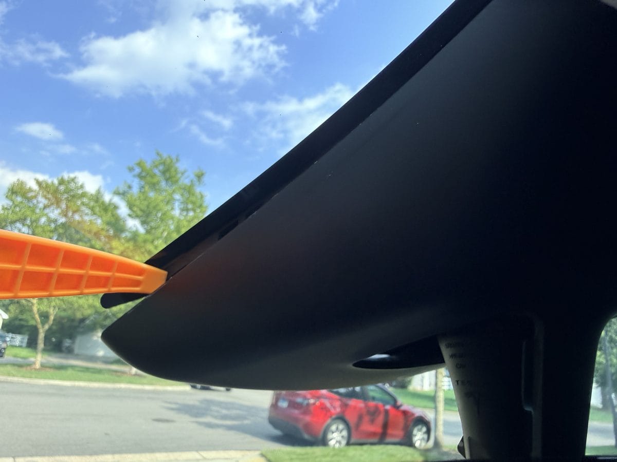 Plastic trim tool working behind the edge of the Tesla camera housing cover