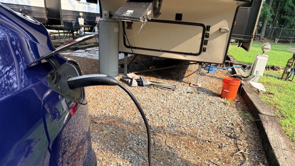 Tesla camping setup: a Model Y plugged in at a campground campsite next to a camper