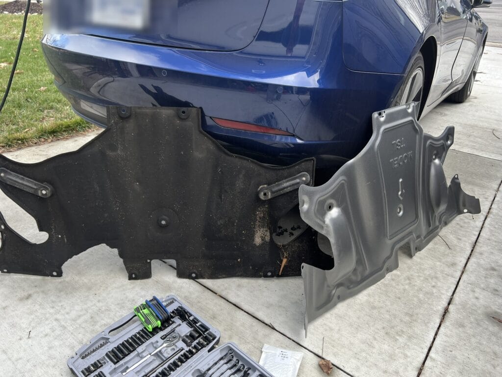 Stock Tesla Model 3 plastic skid plate removed next to aluminum aftermarket replacement