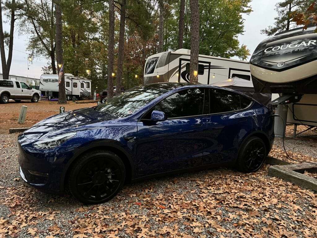 Tesla Model Y charging at a campground next to a fifth-wheel camper