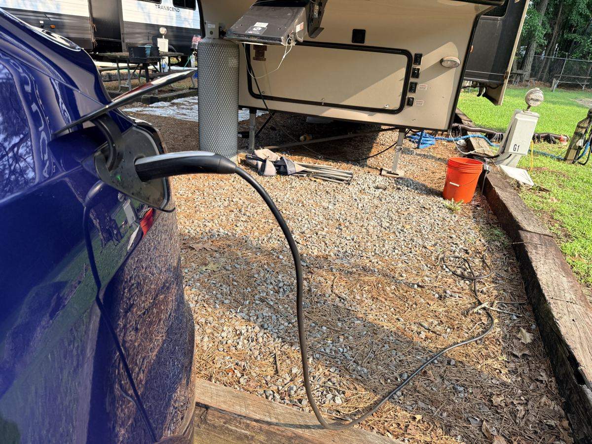 Tesla Model Y plugged in and charging at a campground power pedestal next to a camper