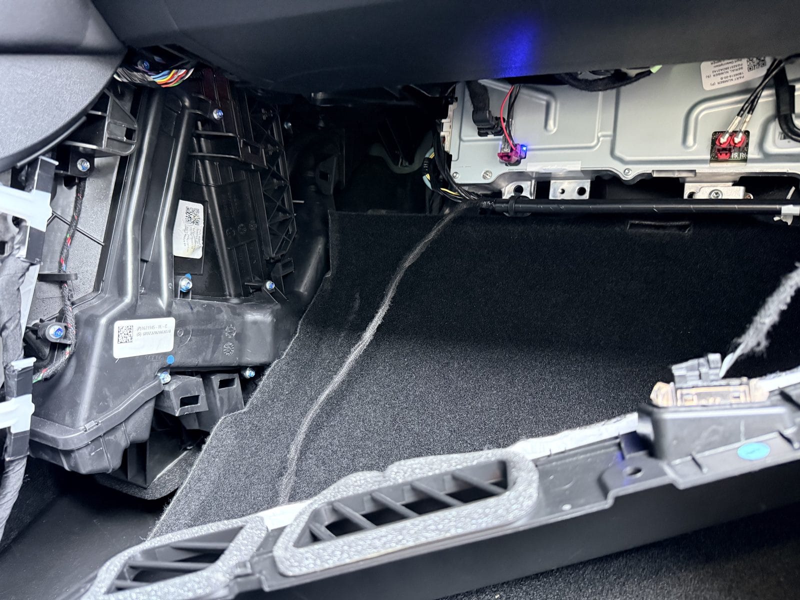 Tesla Model Y passenger footwell with under-glovebox cover removed, showing HVAC housing
