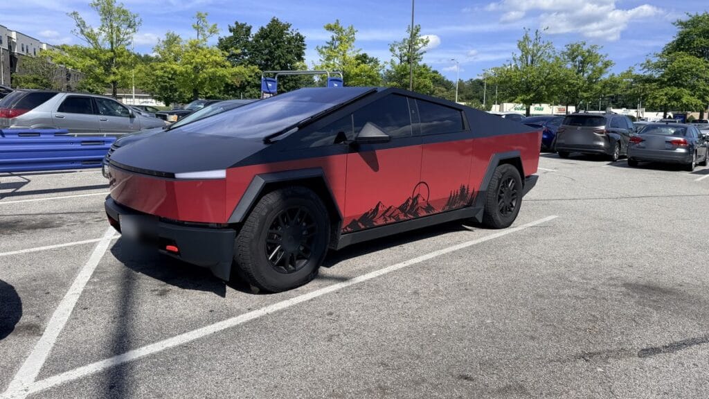 Tesla Cybertruck with a red mountain-scene wrap parked in a lot