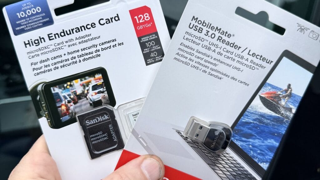 SanDisk High Endurance 128GB microSD card and MobileMate USB 3.0 reader held in hand in front of a Tesla