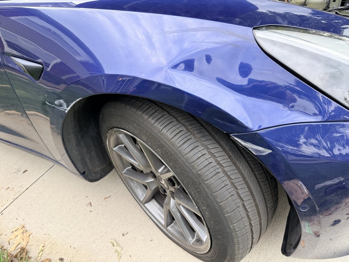 Sideswipe damage on a blue Tesla Model 3 front fender and wheel arch