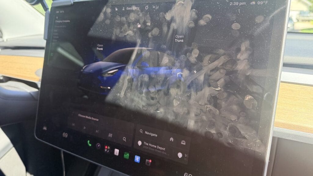 Bare Tesla center touchscreen with fingerprints and glare, illustrating whether you need a Tesla screen protector
