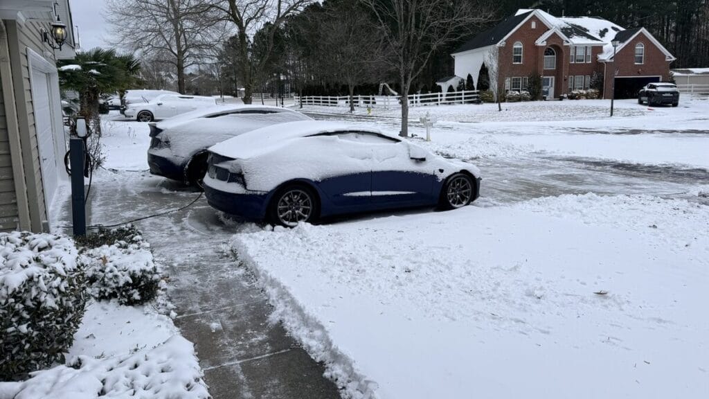 Tesla winter range loss: two snow-covered Teslas plugged in at a home Level 2 charger