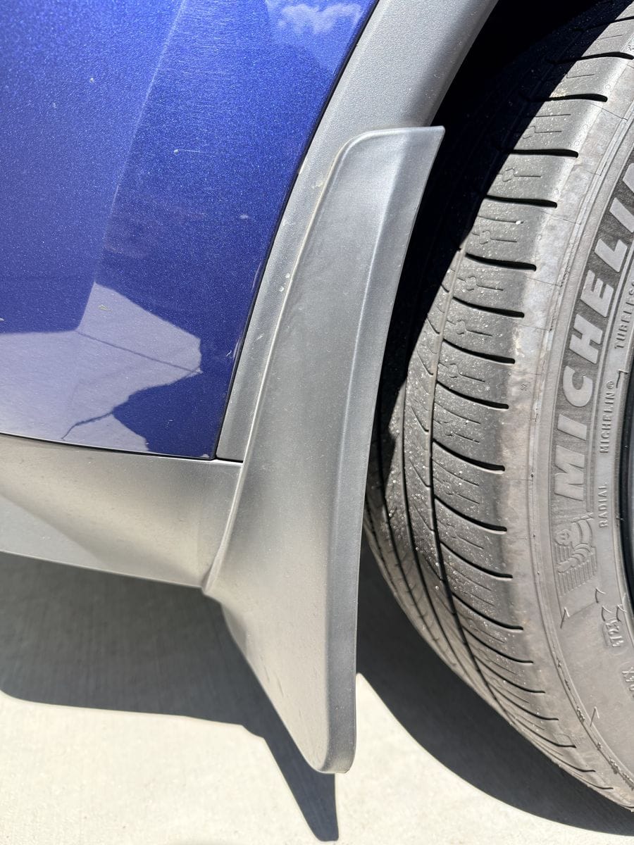 Rigid molded mud flap on a 2023 Tesla Model Y front wheel, sitting tight to the body